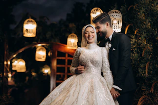 A joyful couple dancing under soft wedding lights with a DJ booth in the background.