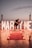 A romantic proposal setting by the sea during sunset. Large illuminated letters spelling 'Marry Me' create a backdrop, surrounded by scattered rose petals and candles on a wooden floor. A couple is captured in a dance pose, adding to the intimate atmosphere.