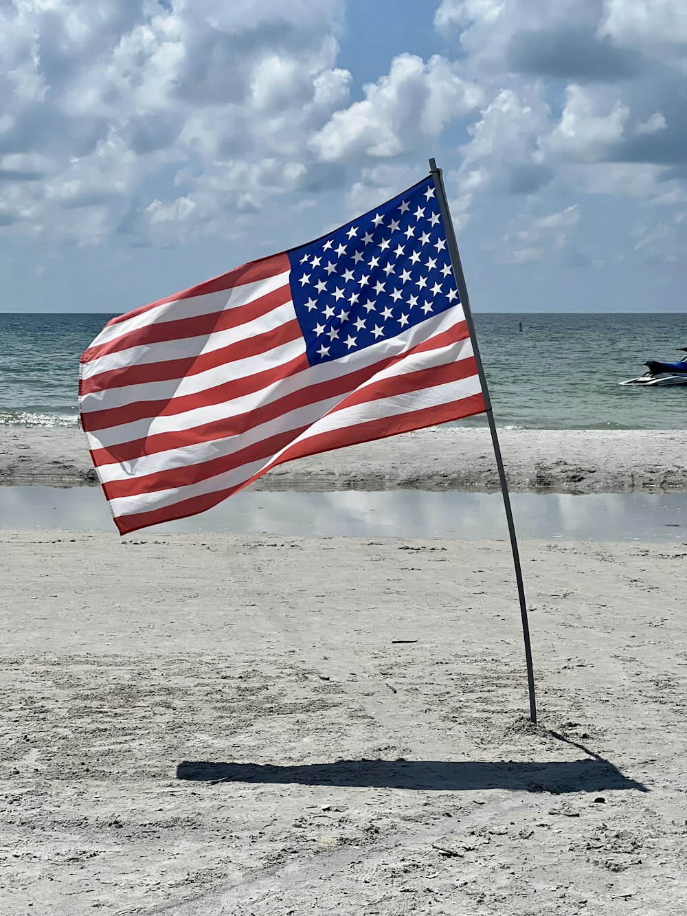 an american flag on a beach with a boat in the background