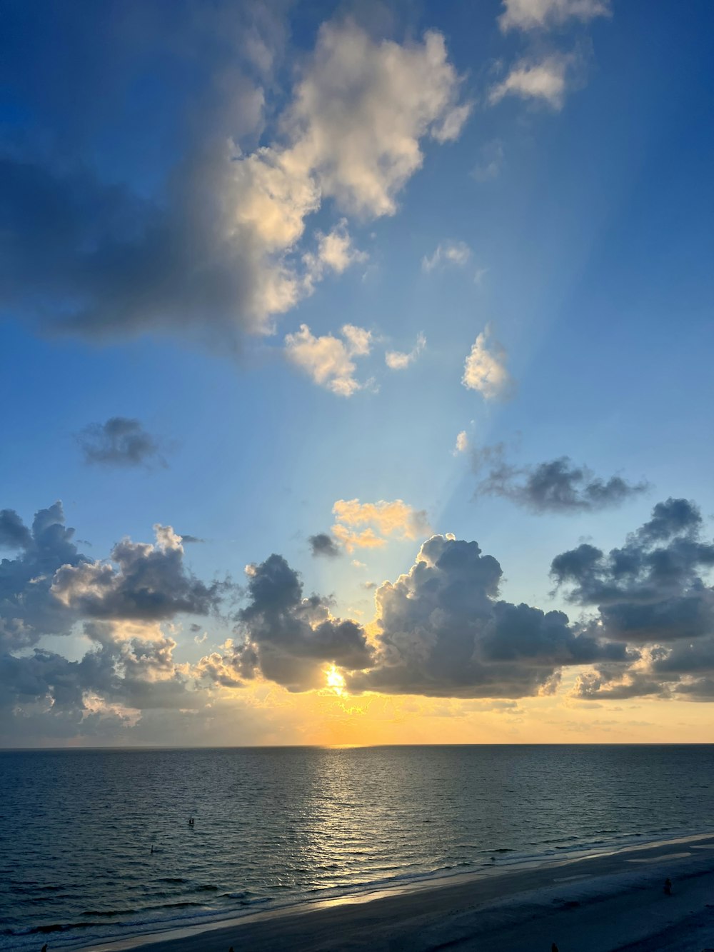 the sun is setting over the ocean on a cloudy day