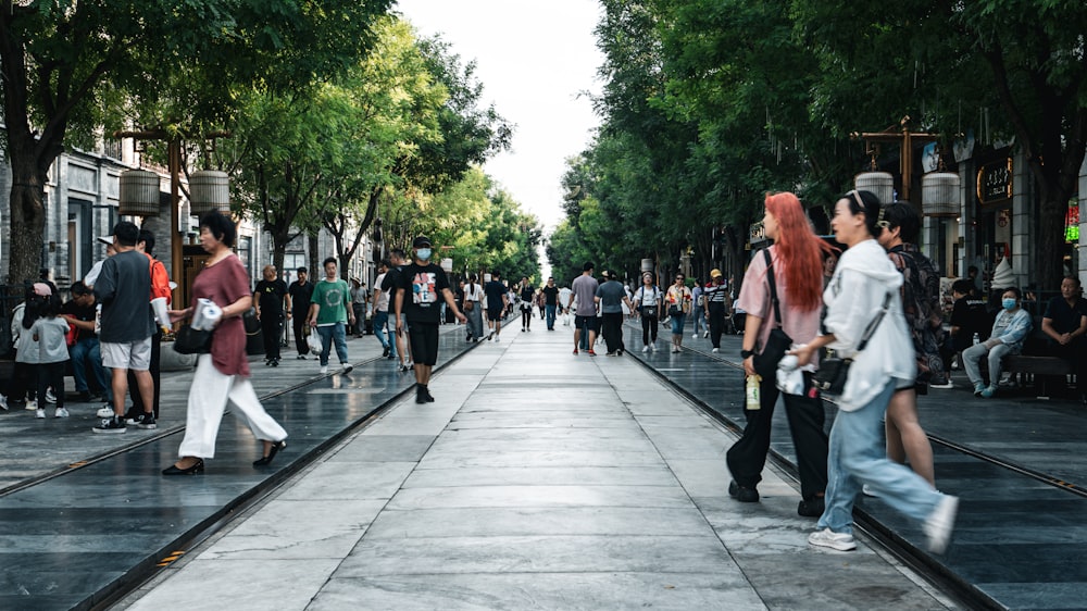 a group of people walking down a street next to trees