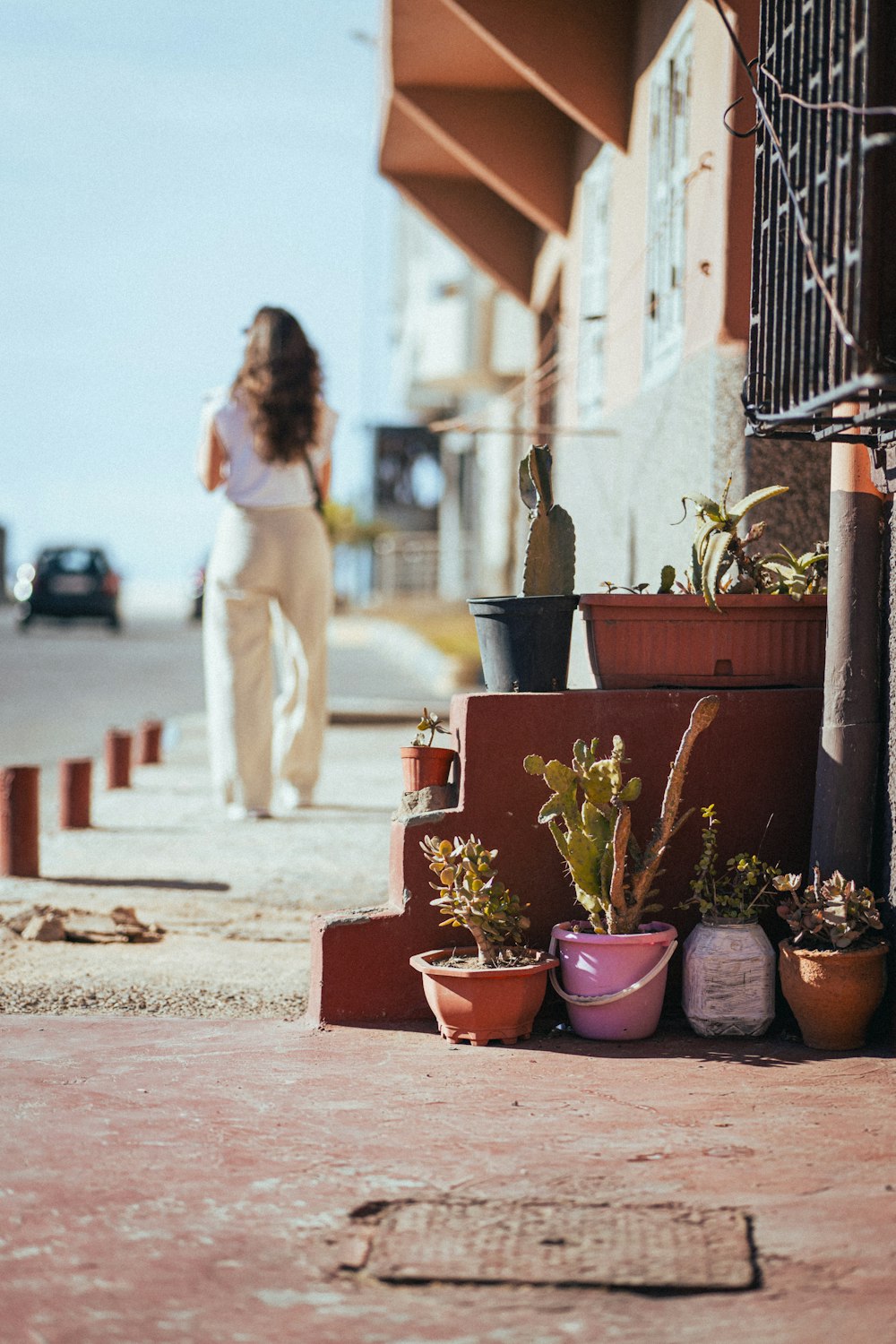 a woman walking down a sidewalk next to potted plants