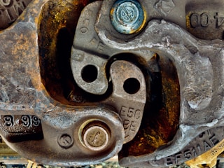 Close-up view of numerous metallic components displaying signs of wear and rust, likely part of machinery or industrial equipment. Several bolts and circular metal pieces with engraved numbers and letters add complexity to the intricate arrangement.