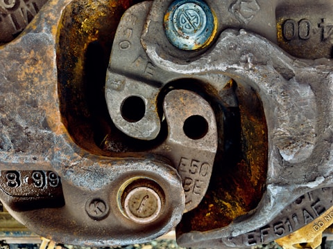 Close-up view of numerous metallic components displaying signs of wear and rust, likely part of machinery or industrial equipment. Several bolts and circular metal pieces with engraved numbers and letters add complexity to the intricate arrangement.