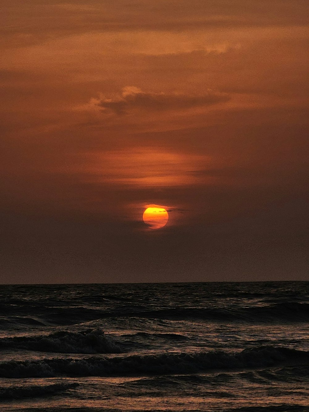 the sun is setting over the ocean on a cloudy day