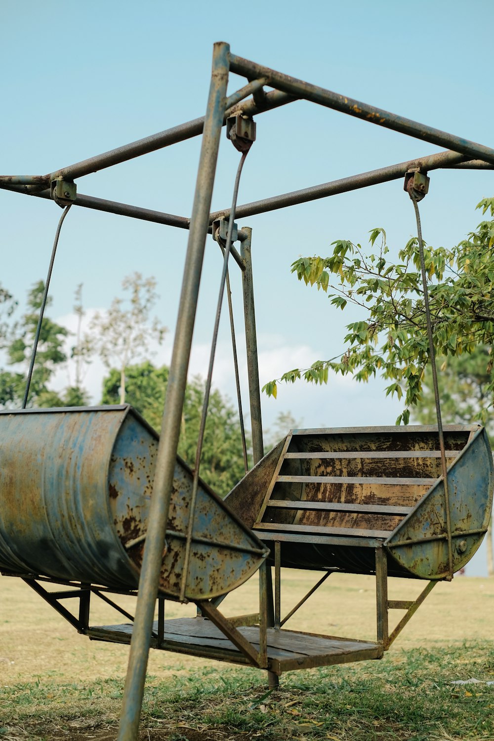 an old rusty metal swing with a tree in the background