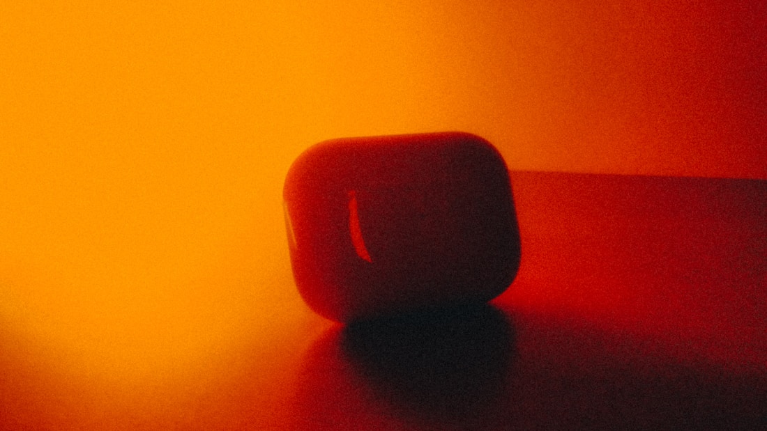 A minimalistic scene featuring a small, rounded object with a glossy surface sitting on a flat surface. Warm and intense lighting in shades of yellow and orange casts dramatic shadows and highlights.