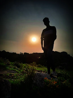 Moody dawn silhouette of a man standing strong in nature, golden light outlining his form.