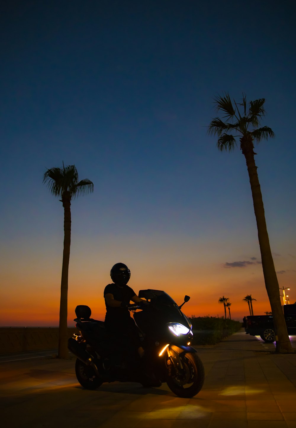 a man riding a motorcycle down a street next to palm trees
