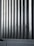 Tall vertical metal slats with a modern architectural design, featuring a series of evenly spaced horizontal lines, creating a sleek and industrial look. In the foreground, there are grey concrete panels at the base which contrast with the metallic texture above.