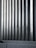 Tall vertical metal slats with a modern architectural design, featuring a series of evenly spaced horizontal lines, creating a sleek and industrial look. In the foreground, there are grey concrete panels at the base which contrast with the metallic texture above.