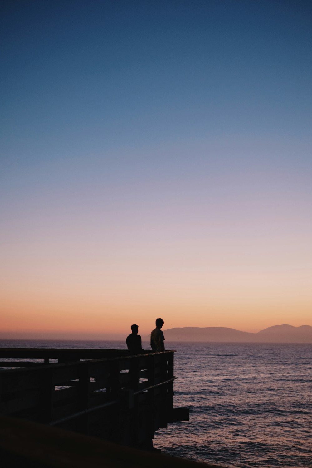 a couple of people sitting on top of a pier