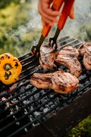 Set of silicone-tipped tongs gripping a juicy grilled steak over a barbecue.