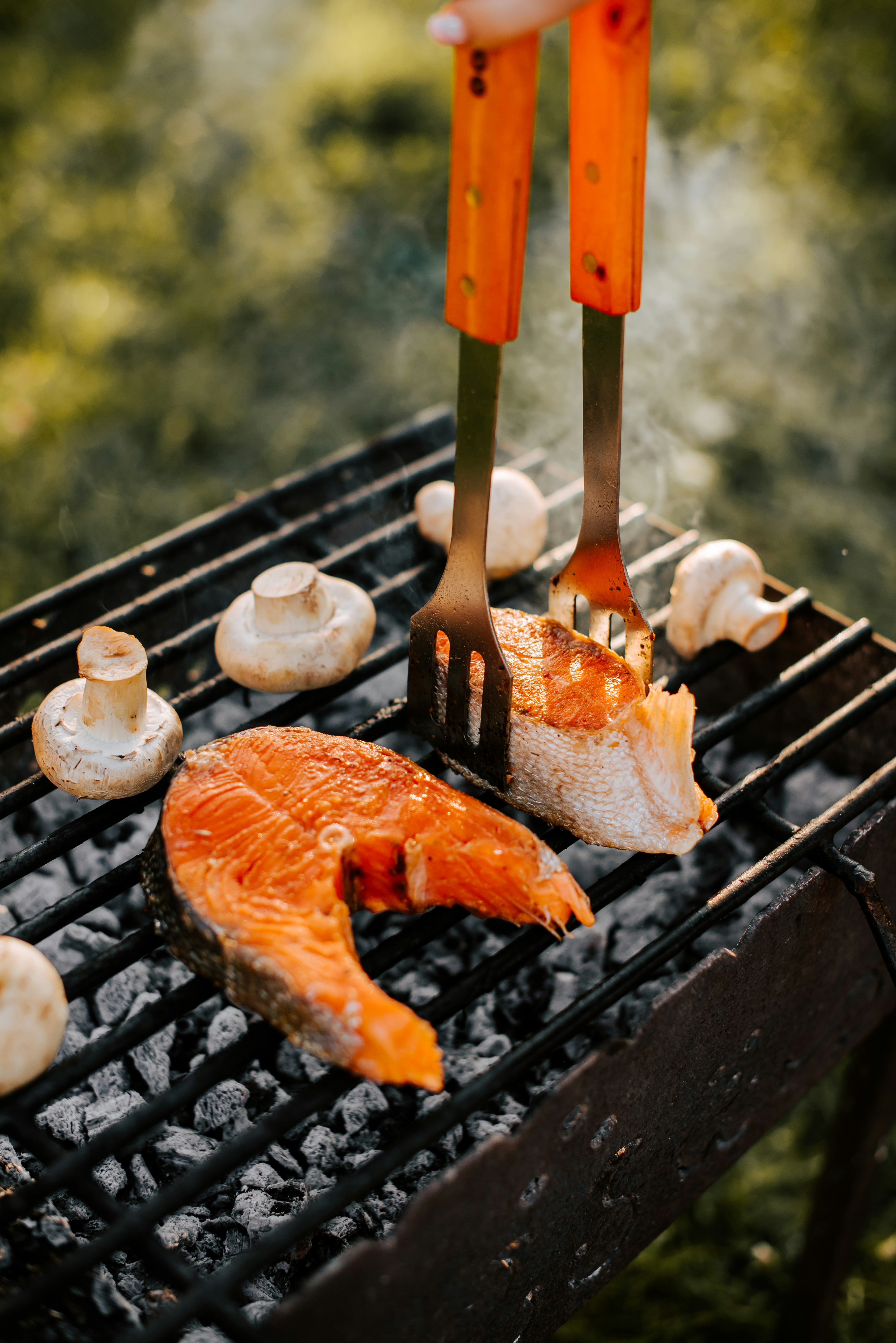Una persona asando salmón en una parrilla con champiñones