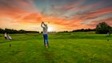 A professional golfer executing a smooth swing on a pristine luxury golf course at sunset