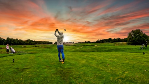A professional golfer executing a smooth swing on a pristine luxury golf course at sunset