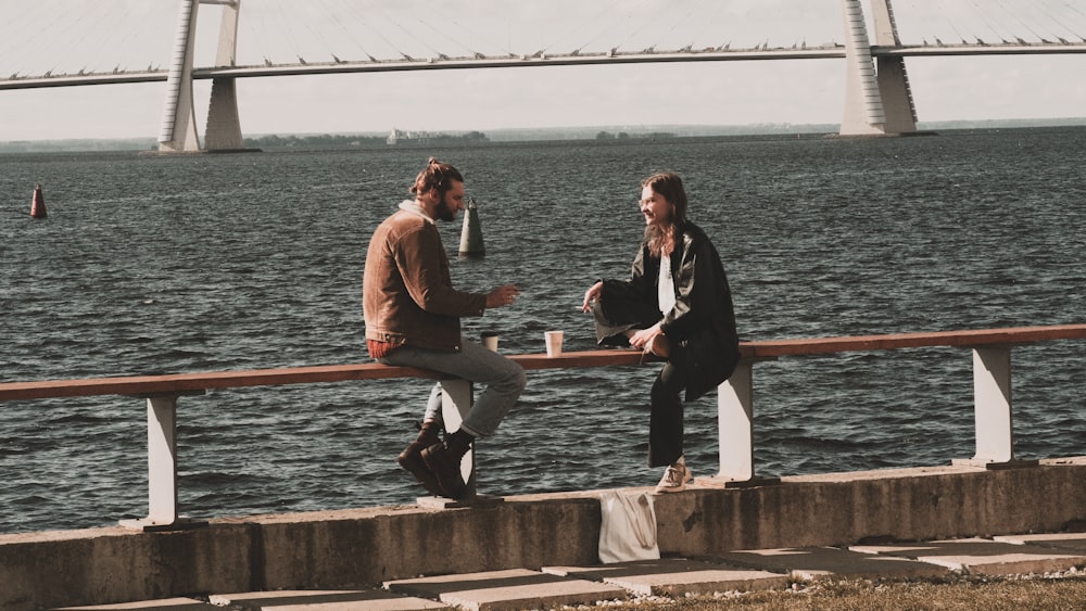 a couple of people sitting on a bench next to a body of water