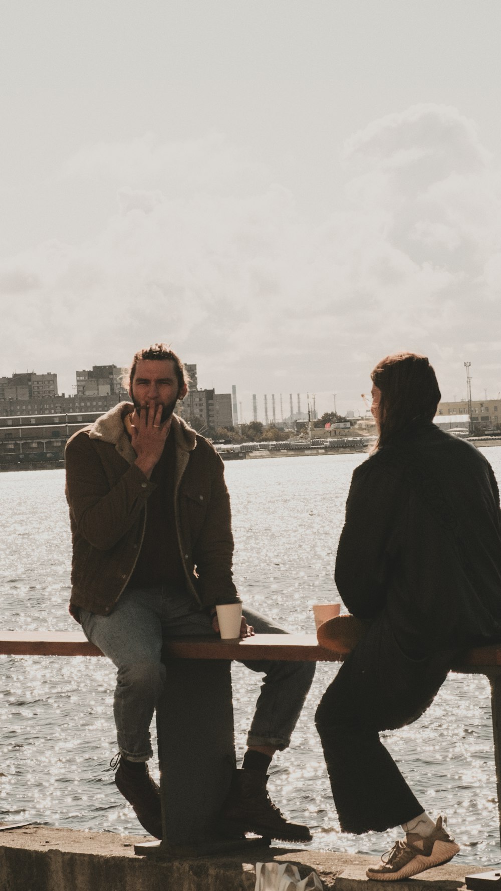 two men sitting on a bench next to a body of water