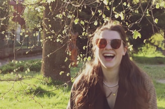 A woman in a flowing dress and oversized sunglasses, laughing under the sun at a café.