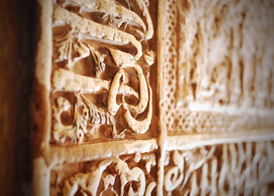 A close-up view of intricate stone carvings with detailed patterns and floral motifs. The surface appears to have a vintage or ancient look, suggesting it might be part of historical architecture or a monument.
