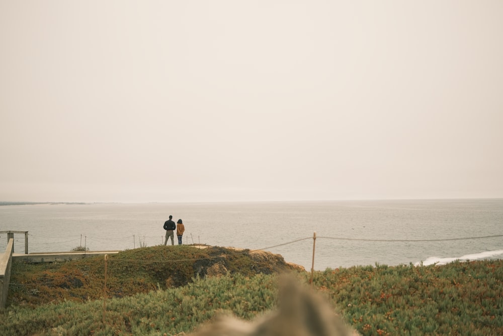 two people standing on a hill overlooking the ocean