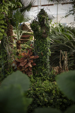 A peaceful garden corner featuring a planter tower and an iron statue surrounded by lush foliage.