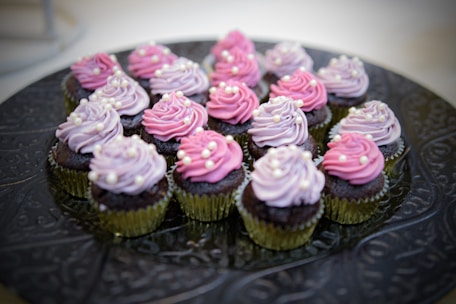 A vibrant display of pink and gold frosted cupcakes arranged on a shiny gold platter.