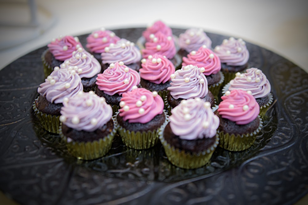 a black plate topped with cupcakes covered in frosting