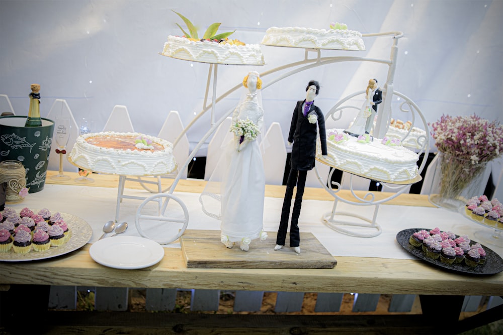 a table topped with cakes and cupcakes with a bride and groom figuri