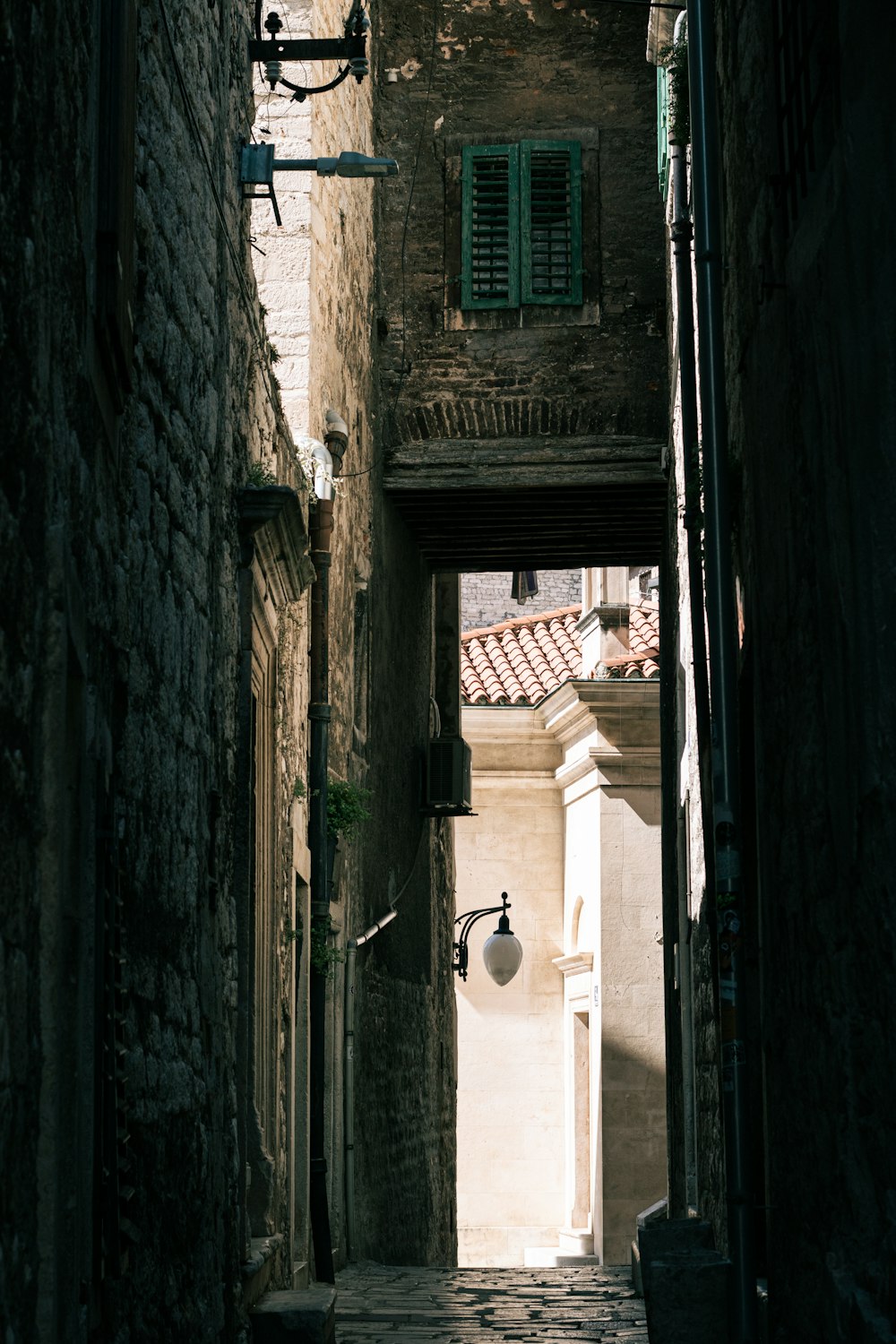 a narrow alley way with a lamp post and shutters