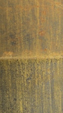 A textured surface with a blend of rust and yellowish hues creates a weathered appearance. The rust stains form irregular patterns and vertical streaks across the surface, evoking an aged and industrial look.