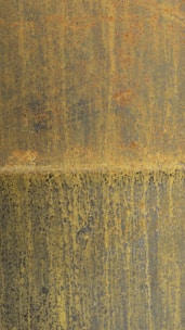A textured surface with a blend of rust and yellowish hues creates a weathered appearance. The rust stains form irregular patterns and vertical streaks across the surface, evoking an aged and industrial look.