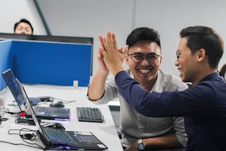 two men sitting at a table with a laptop