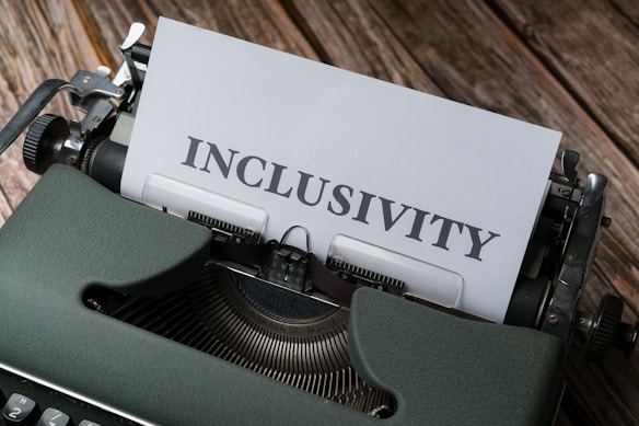 A vintage typewriter with a piece of paper loaded into it displaying the word 'inclusivity'. The typewriter is placed on a wooden surface, suggesting a rustic or nostalgic setting.