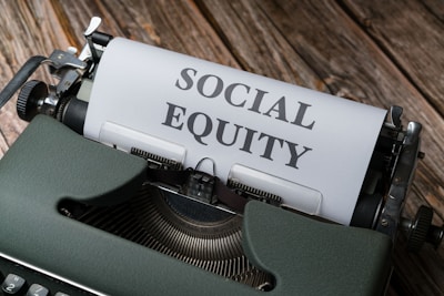 A vintage typewriter with a sheet of paper that has the words 'SOCIAL EQUITY' typed in bold letters. The typewriter is placed on a rustic wooden surface.