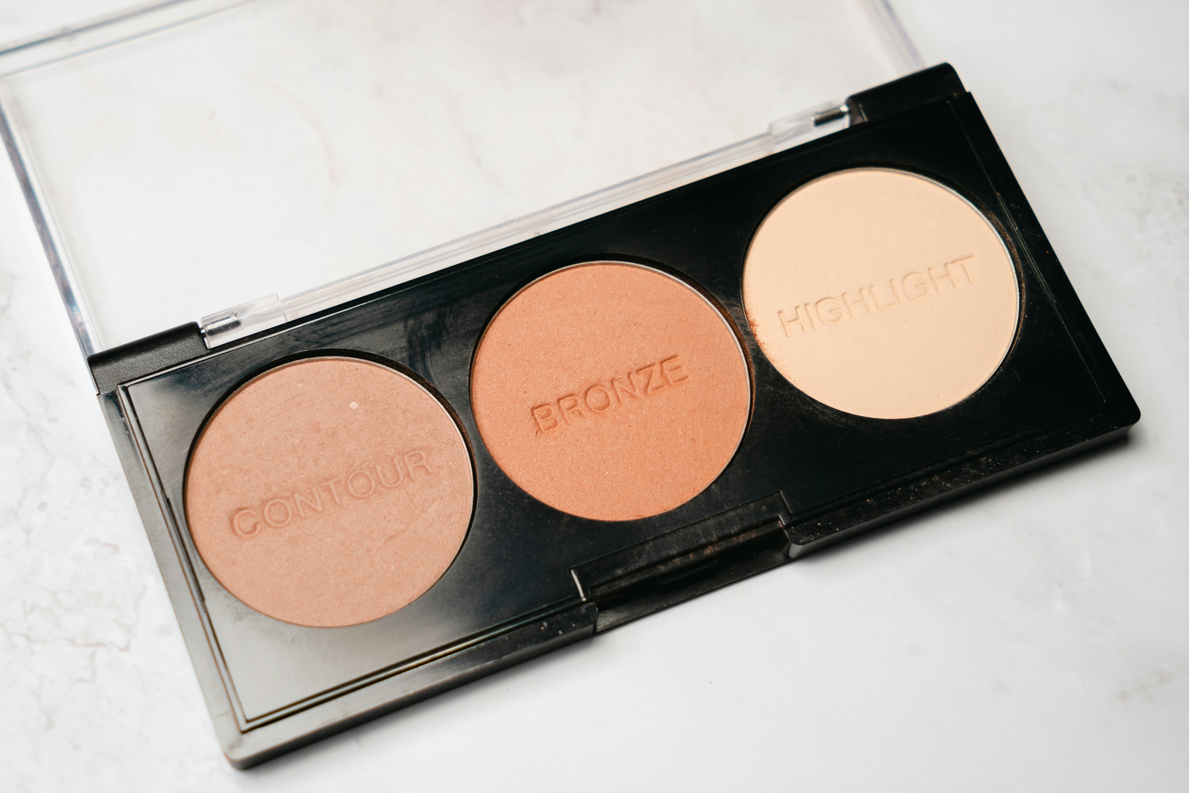 Professional contour and highlight makeup palette with warm bronze tones on pink background