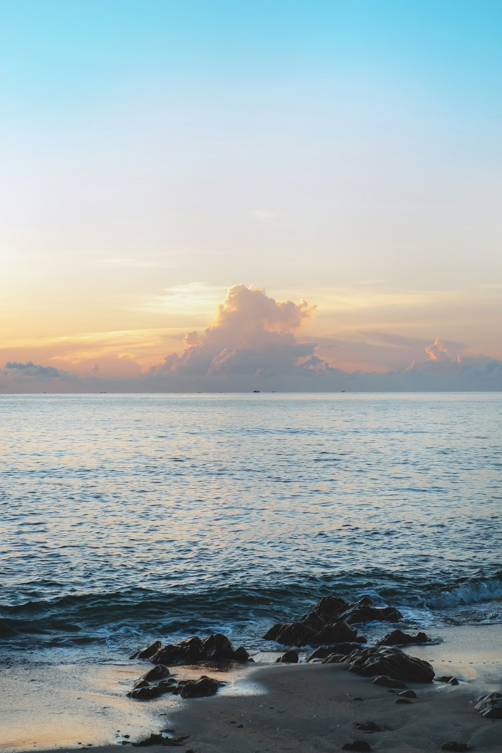 the sun is setting over the ocean with rocks in the foreground