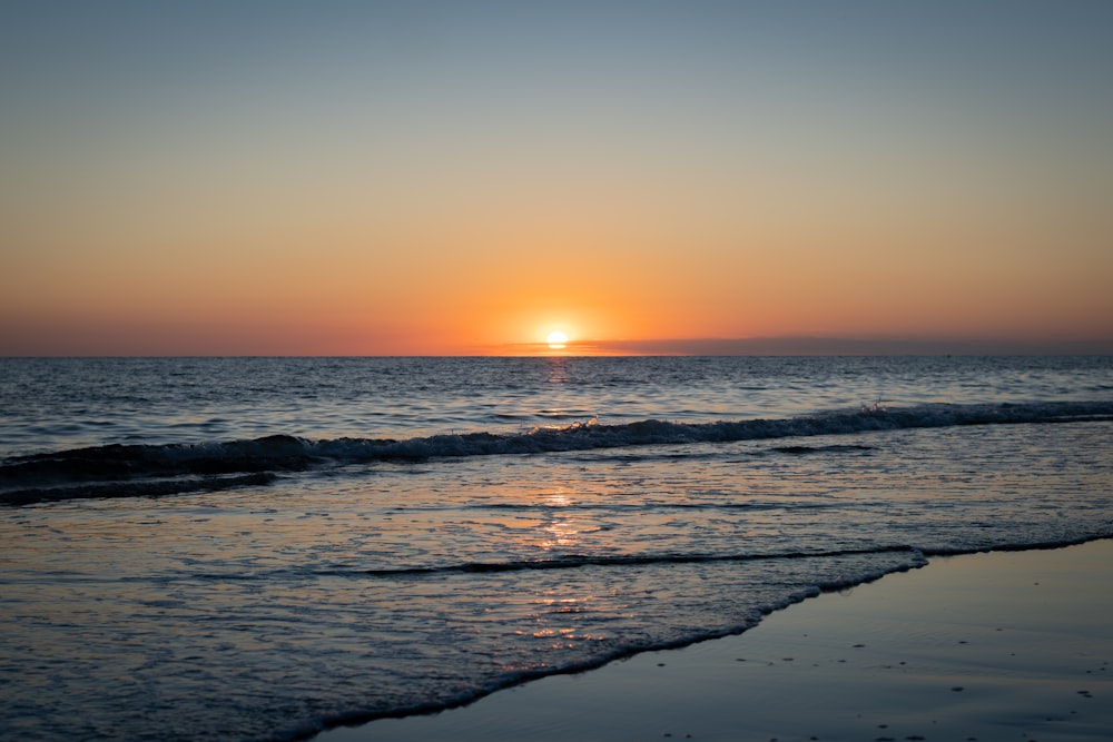 the sun is setting over the ocean on a beach