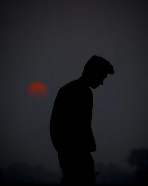 A silhouette of a lone figure standing on a cliff against a blood-red moon.