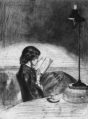 A person is sitting at a table, deeply engaged in reading a book. The setting is dimly lit, with an oil lamp providing illumination. The atmosphere is intimate and quiet. A cup, possibly of tea or coffee, is placed on the table next to the person.