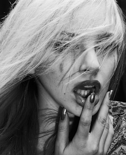 A moody shot of a woman's hand gently touching her lips, with deep shadows and warm skin tones.