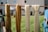 Four skeins of yarn hang over a wooden rod. Two are a golden brown color and the other two are a light cream color. The setting is an outdoor area with a grassy lawn and part of a building visible in the background.