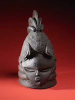 An ornate African mask displayed against a warm, earthy backdrop.
