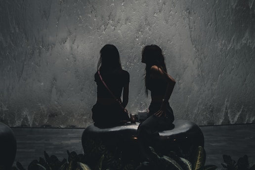 two women sitting on stools in front of a fountain