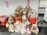A large collection of trash and recycling items is piled up, consisting of cardboard boxes, plastic containers, and various packaging. The waste is overflowing from two large orange bins with pink signs above them, indicating different types of waste.