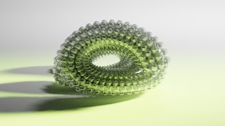 A symmetrical, translucent green structure composed of interconnected spherical elements forms a torus-like shape. The background is softly lit with a gradient of pale green and white, casting subtle shadows underneath the structure.