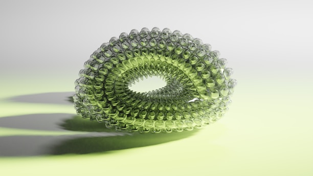 A symmetrical, translucent green structure composed of interconnected spherical elements forms a torus-like shape. The background is softly lit with a gradient of pale green and white, casting subtle shadows underneath the structure.
