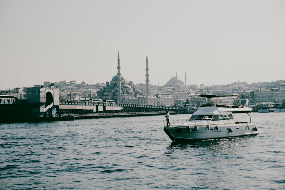 The image depicts a serene scene on the Bosphorus strait, with two boats floating side by side. The boat on the left is white and appears to be a yacht or a similar vessel, while the one on the right is gray and seems to be a larger ship.

In the background, there are several buildings visible, including a mosque with minarets that can be seen in the distance. The sky above is overcast, casting a soft light over the scene.