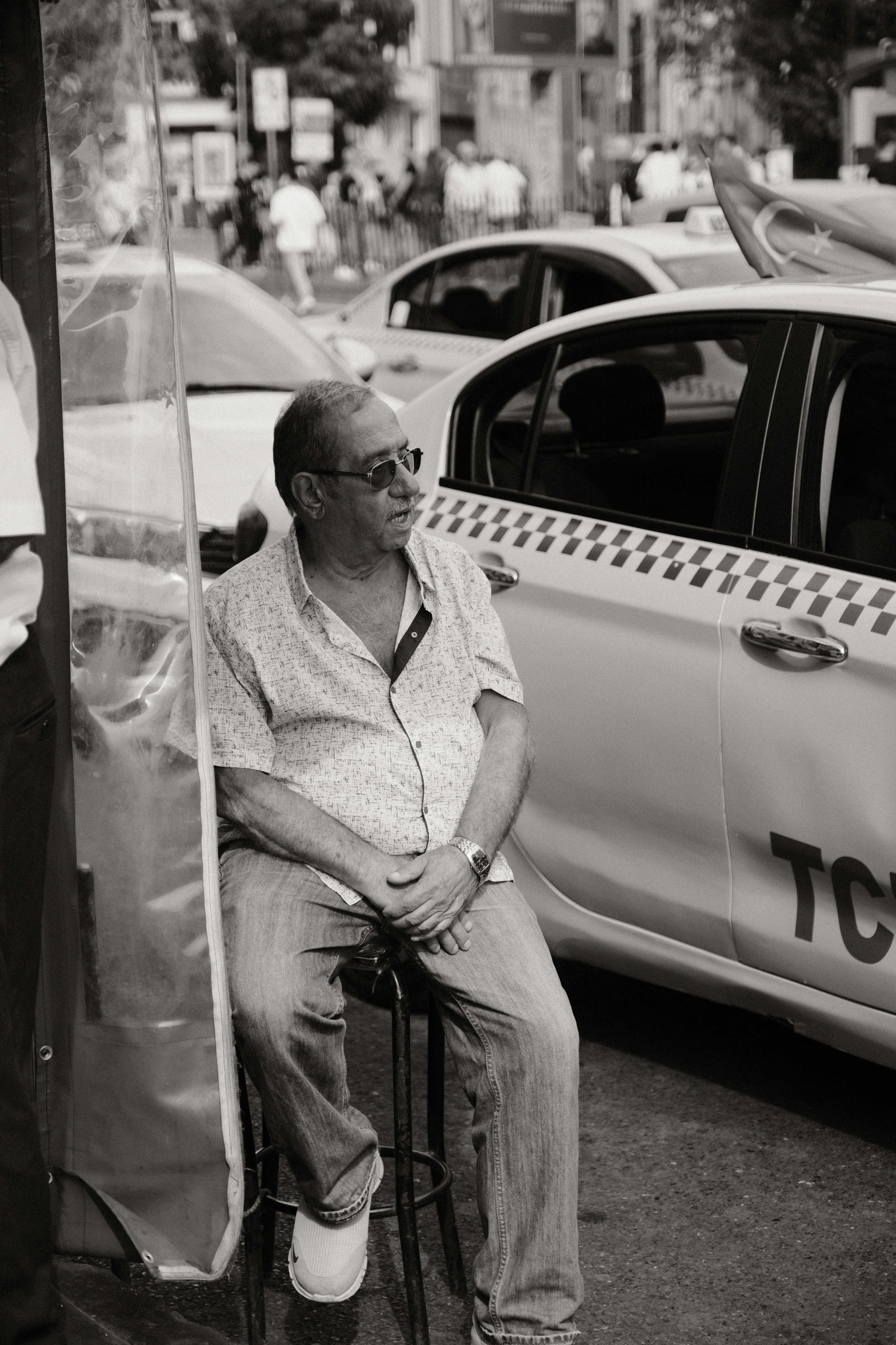 a man sitting on a stool in front of a taxi cab