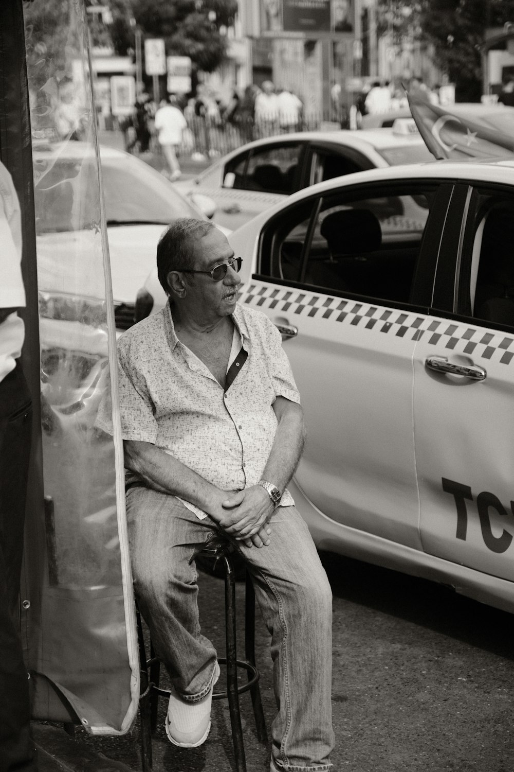 a man sitting on a stool in front of a taxi cab